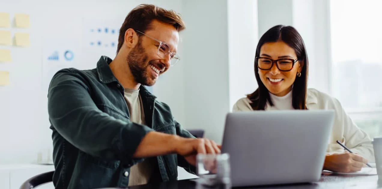 Duas pessoas olhando para o notebook na empresa A imagem tem duas pessoas, um homem e uma mulher, eles estão olhando para o notebook, enquanto trabalham.